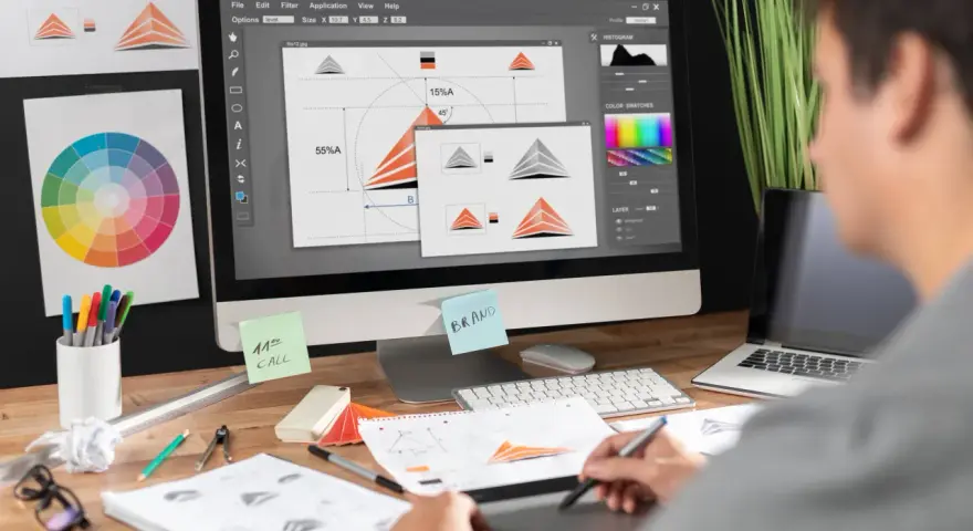 Diseñador gráfico trabajando en un logo, con paleta de colores y bocetos. Imágenes libres de derecho de autor.
