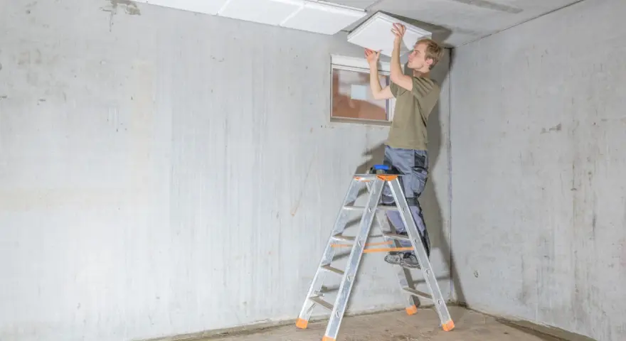 Mann auf Leiter montiert weiße Platten zur kellerdecke isolieren.