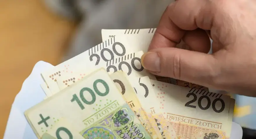 Dłoń trzyma banknoty 100 i 200 zł. Czy to już zapowiedź podwyżki najniższej krajowej 2026?