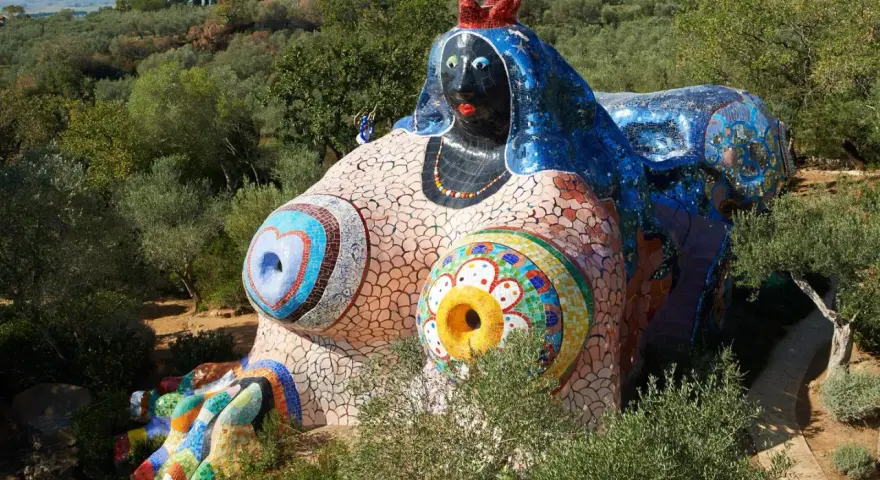 Œuvres d'art de Niki de Saint Phalle : une sculpture monumentale et colorée, représentant une femme allongée, ornée de mosaïques vives, dans un paysage verdoyant.
