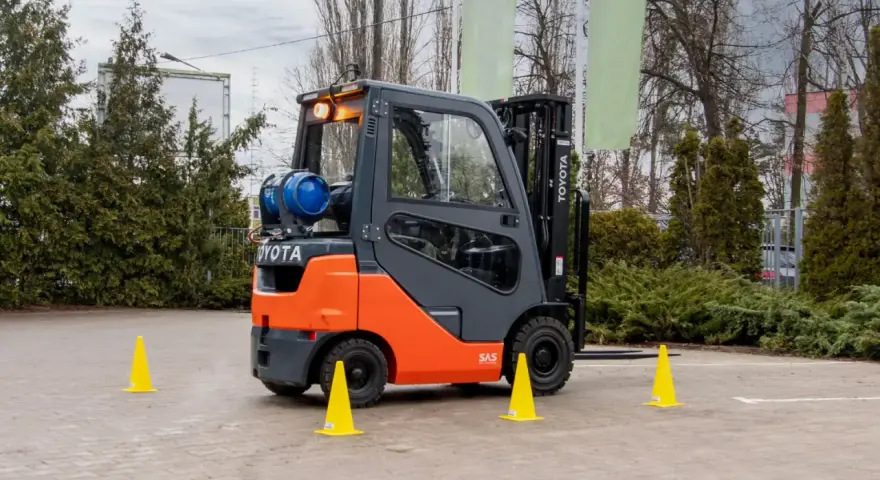 Pomarańczowo-szary wózek widłowy Toyota z butlą gazową, otoczony żółtymi pachołkami, gotowy do testów UDT.