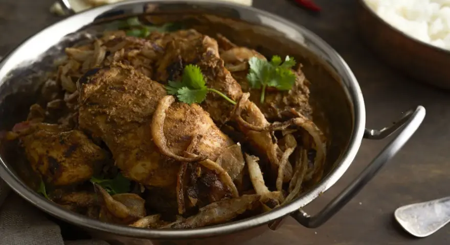 Kurczak w sosie garam masala z cebulą i kolendrą w metalowej misie.