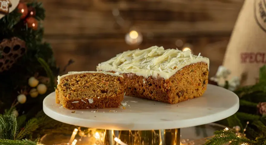 Pyszny, wilgotny naked cake marchewkowy z kremem i wiórkami białej czekolady, udekorowany świątecznymi światełkami i gałązkami choinki.