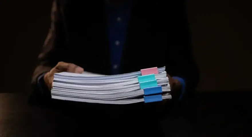 Mężczyzna w garniturze trzyma stos dokumentów z kolorowymi spinaczami. Może to być materiał dowodowy w sprawie hipoteka przymusowa.