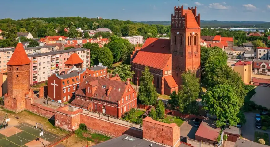 Zamek krzyżacki w Lęborku, z charakterystyczną wieżą i ceglanymi murami, góruje nad miastem. Obok widać kościół i zabudowania.