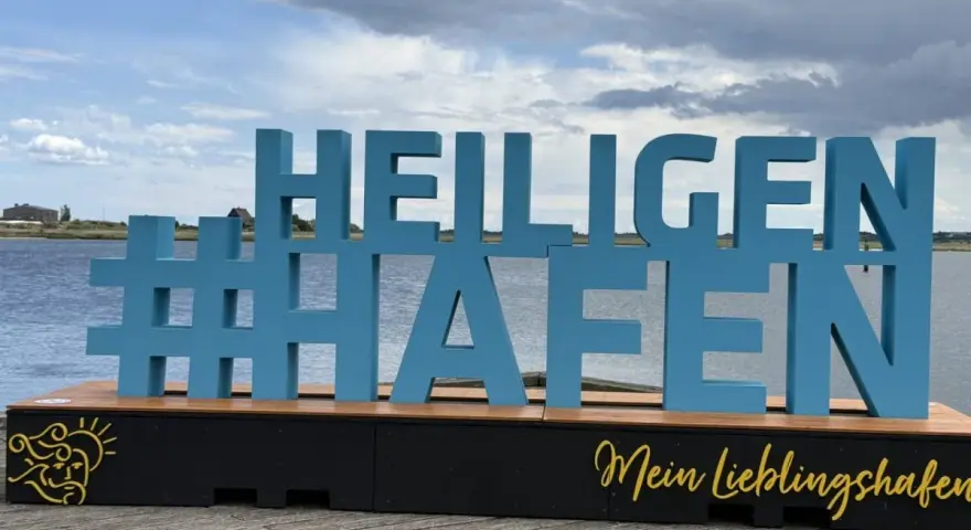 Große blaue Buchstaben mit #Heiligenhafen auf einem Holzpodest. Perfekt für Ausflugsziele und Erinnerungen an diesen schönen Ort.
