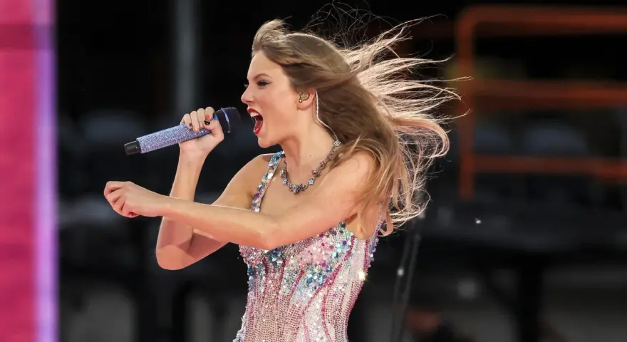 Taylor Swift w błyszczącej sukience śpiewa na koncercie w Warszawie, włosy rozwiane przez wiatr.
