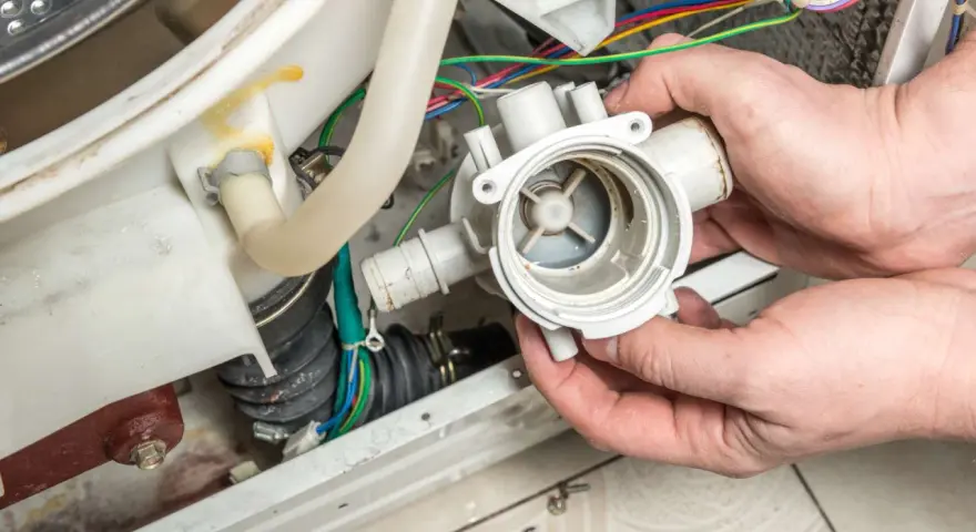 Hände halten eine Waschmaschine-Pumpe, die nicht abpumpt. Kabel und Schläuche sind sichtbar.