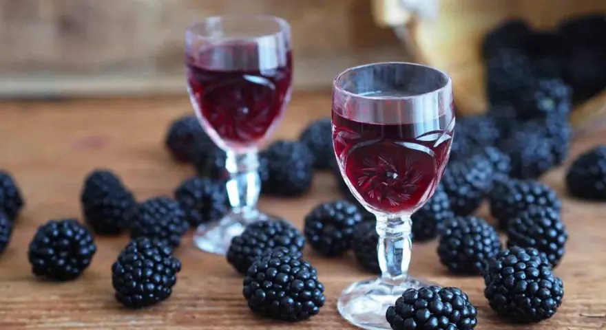 Dwa kieliszki z rubinową nalewką z jerzyn, otoczone świeżymi owocami na drewnianym blacie.