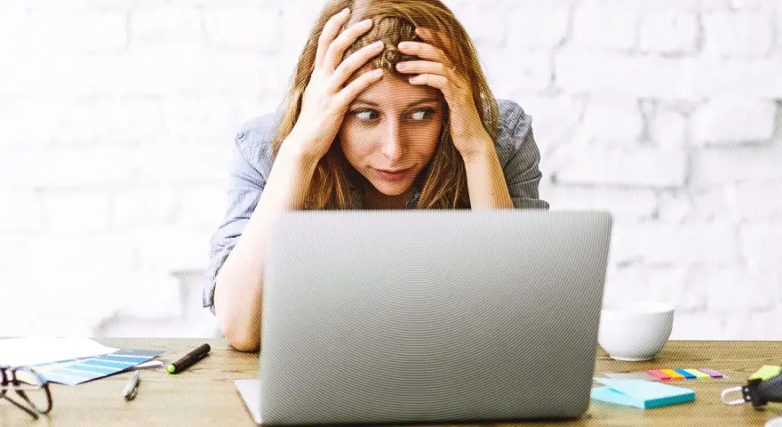 Verzweifelte Frau mit Händen in den Haaren, die auf einen Laptop starrt. Die Website-Migration scheint sie zu überfordern.