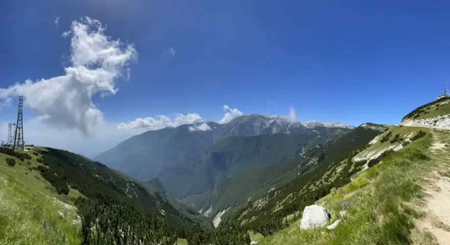 Panoramica mozzafiato sui monti dell'Abruzzo, con un sentiero che sale verso un **block house** e torri di trasmissione.