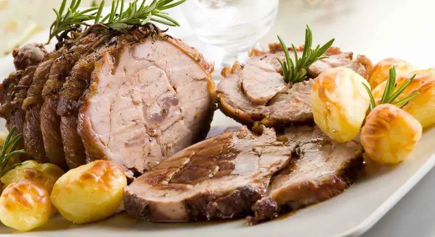Succulento arrosto di vitello affettato, guarnito con rosmarino e accompagnato da patate arrosto dorate.