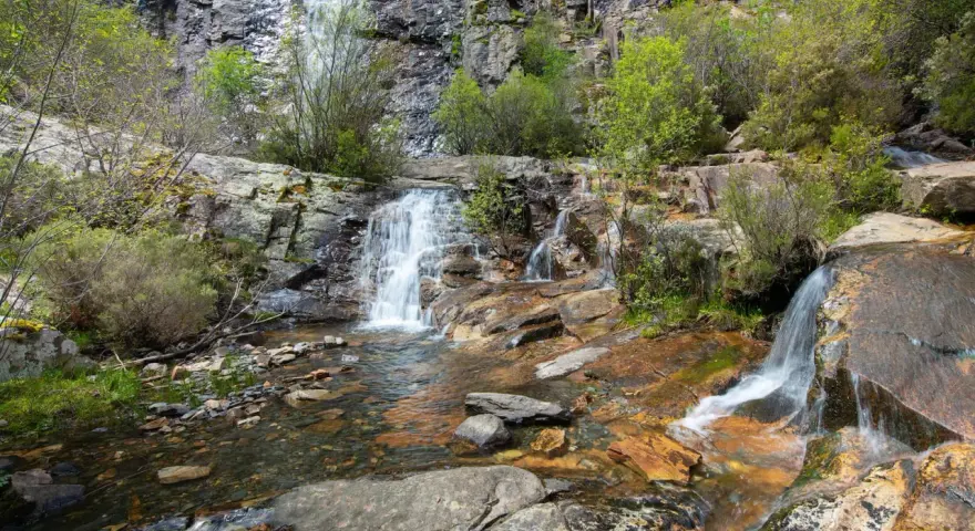Las chorreras de despeñalagua, cascadas de agua blanca cayendo sobre rocas rojizas y verdes arbustos en un paisaje rocoso.