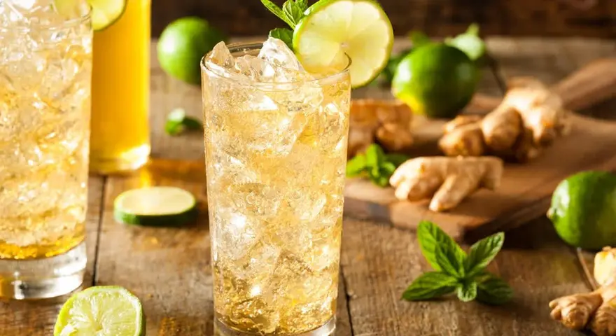 En uppfriskande ginger beer drink med is, lime och mynta. Ingredienser som ingefära och lime ligger utspridda.