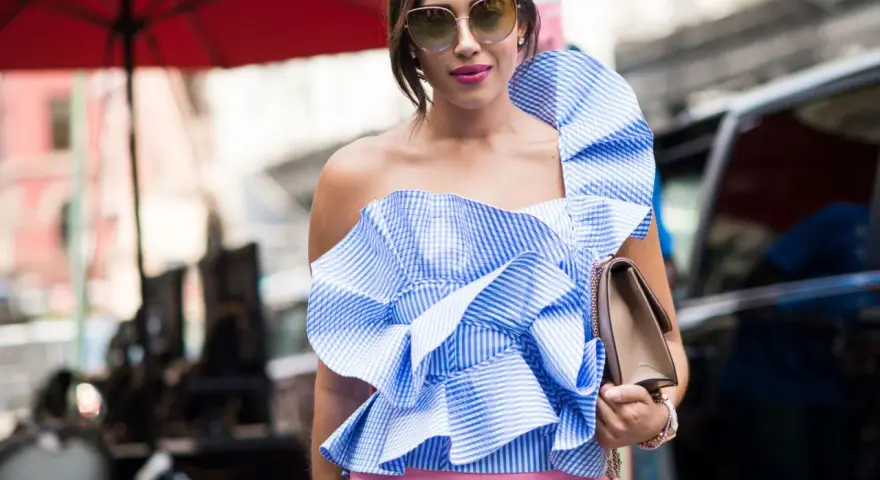 Eleganza in **abbinamento rosa e blu**: top a balze a righe azzurre e bianche con pantaloni rosa cipria, occhiali da sole e borsa a tracolla.