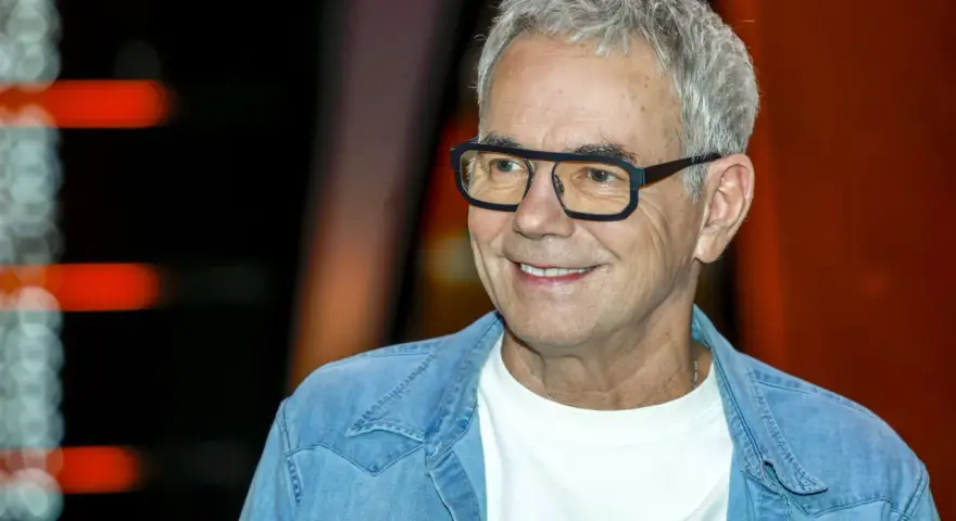 Uśmiechnięty mężczyzna w okularach, w jeansowej koszuli, jakby czekał na pytanie: "Jaka to melodia?".