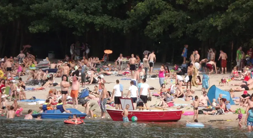 Tłum ludzi odpoczywa na plaży nad jeziorem w Jelczu Laskowicach. Słońce, piasek i woda tworzą idealne warunki do letniego relaksu.