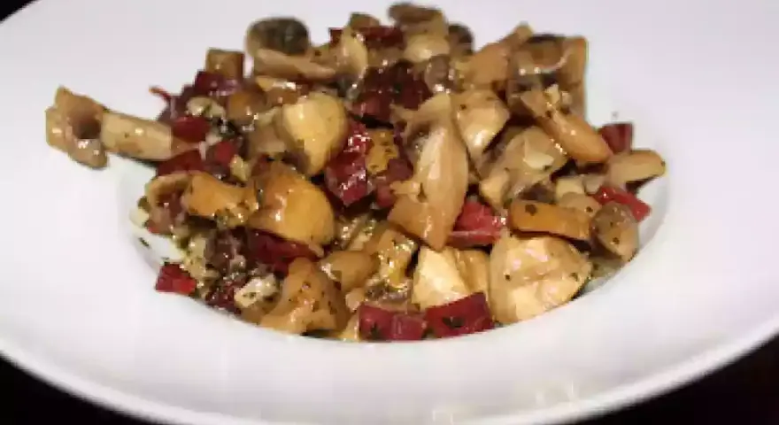 Champiñones salteados con trocitos de jamón, servidos en un plato blanco. Un plato sencillo y sabroso.