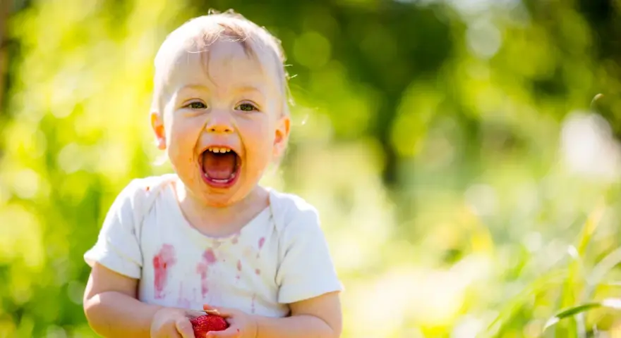 Uśmiechnięte 1.5 roczne dziecko nie mówi mama, ale z radością trzyma truskawkę.
