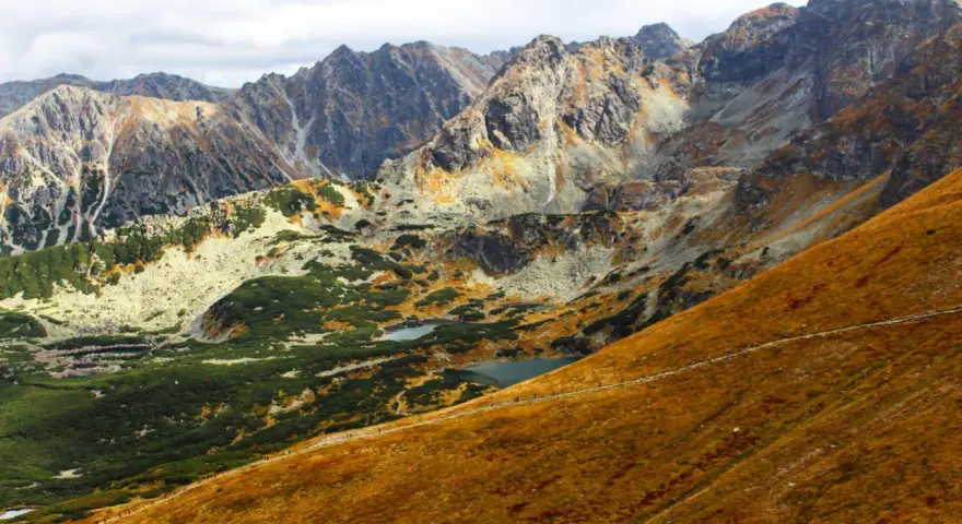 Widok na Tatry jesienią. Widać szlak turystyczny, którym idzie się na Kasprowy, małe stawy i skaliste szczyty.