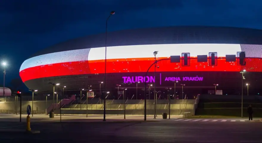 Tauron Arena Kraków nocą, z podświetloną fasadą w barwach narodowych. Obiekt mieści 15 tysięcy widzów, co czyni go jednym z największych w Polsce.