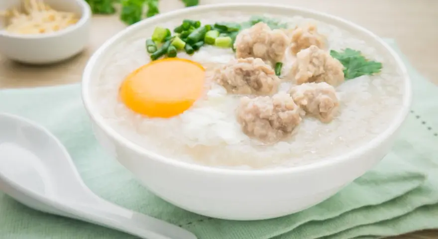 Miseczka pysznego congee z mięsnymi klopsikami, jajkiem i szczypiorkiem. Idealne na rozgrzewający posiłek.