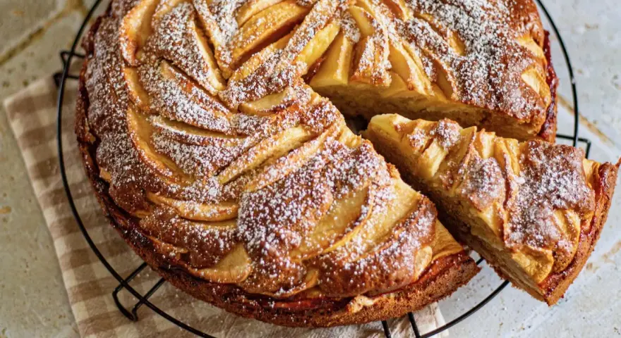 Gâteau mascarpone pommes, une tranche coupée, saupoudré de sucre glace. Un délice doré et moelleux.