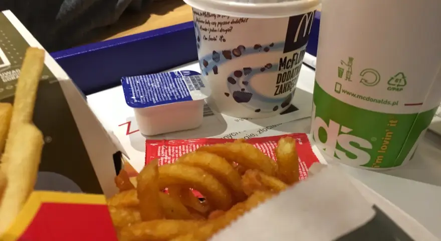 Zakręcone frytki McDonald's w pudełku z sosem i napojem.