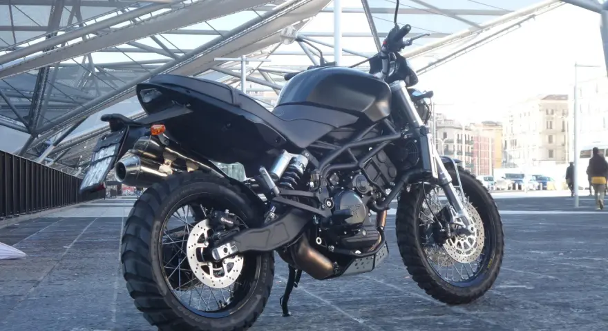 La Moto Morini Scrambler 1200, nera e imponente, si staglia sotto una struttura metallica moderna.