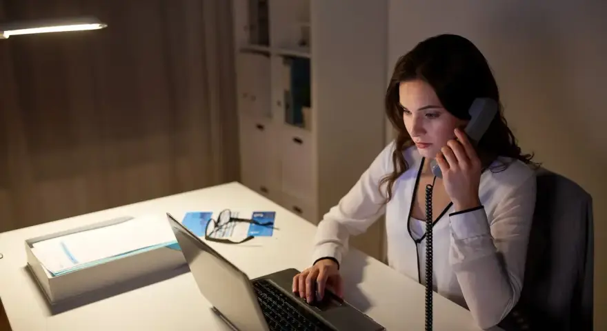 Młoda kobieta, dyspozytor, pracuje po godzinach przy laptopie i telefonie.
