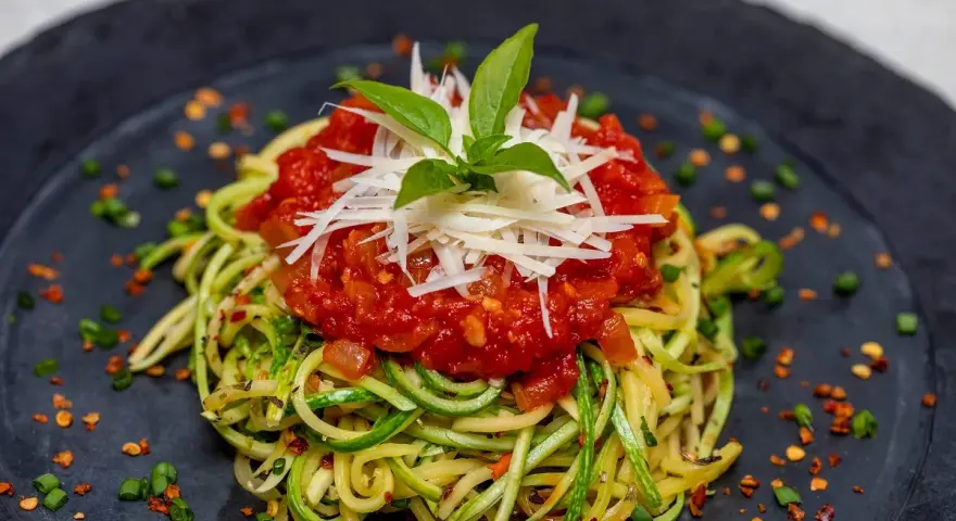Deliciosa pasta con verduras, hecha de calabacín en espiral, cubierta con salsa de tomate y queso rallado.