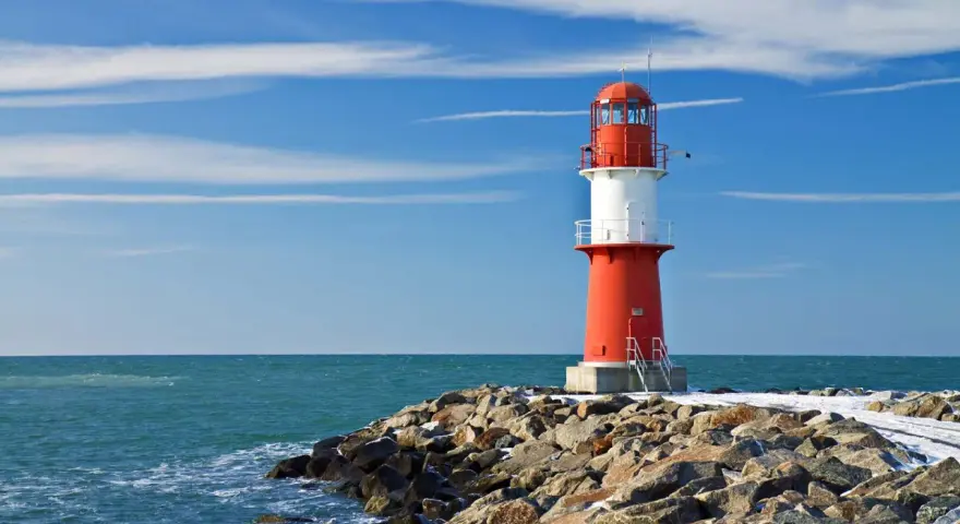Roter Leuchtturm auf felsiger Mole am barth strand. Blaues Meer und Himmel mit Wolken.