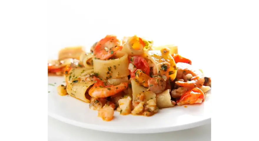 Piatto di calamarata allo scoglio con gamberi, cozze e pomodorini, condita con prezzemolo fresco.