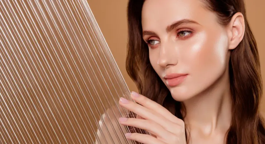 Kobieta z idealną cerą, która emanuje blaskiem, niczym efekt glass skin. Delikatne linie na pierwszym planie dodają głębi.