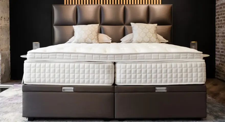 Lit, deux matelas blancs sur des sommiers marron. Le matelas trop grand pour sommier crée un léger débord.