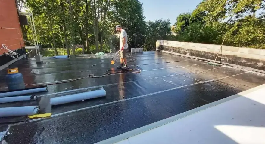 Pracownik wykonuje układanie płyt tarasowych na suchym betonie, używając palnika do obróbki papy.