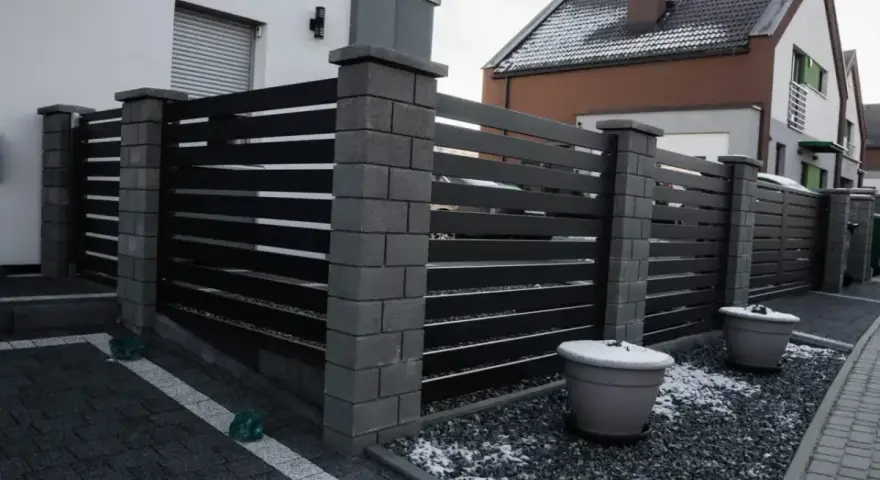 Nowoczesne ogrodzenie z betonowych słupków i ciemnych paneli. Taka wysokość ogrodzenia bez pozwolenia zapewnia prywatność.