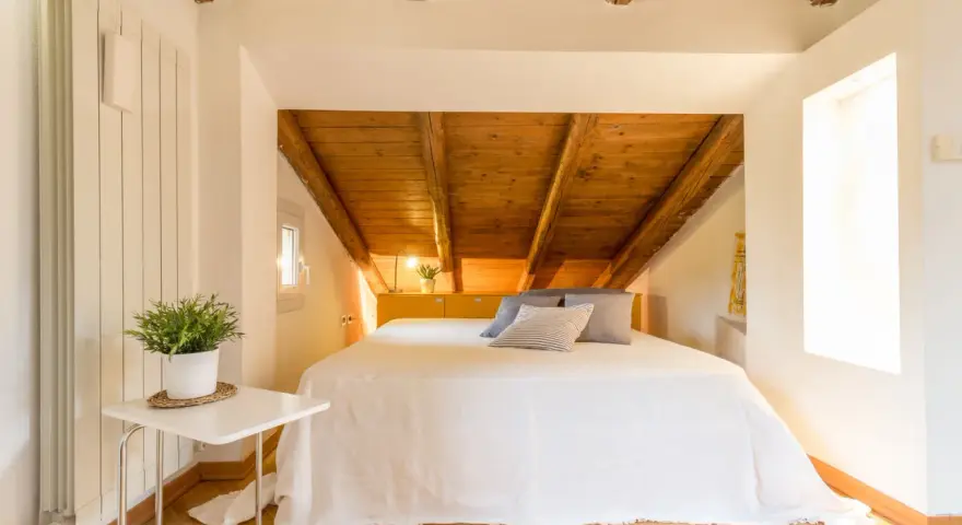 Accogliente camera da letto in mansarda con travi a vista in legno. Idee per un nido romantico e funzionale.