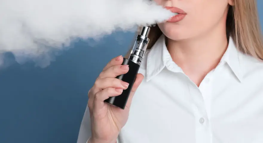 Mujer exhala vapor de un vaper, una alternativa moderna al tabaco tradicional.