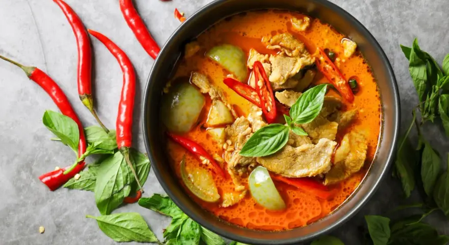 Miseczka czerwonego curry z mięsem, warzywami, papryczkami chili i bazylią.