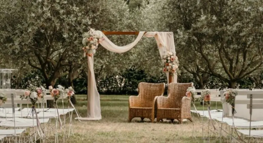 Un décor champêtre pour une célébration laïque : chaises blanches, arche fleurie, fauteuils en rotin sous les oliviers.