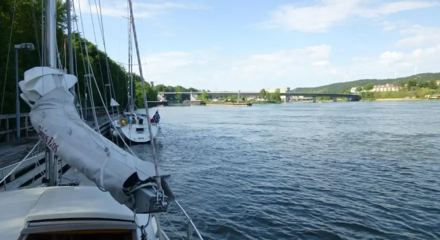 Segelbåtar vid kaj i Lilla Edet, en bro syns i bakgrunden över en bred flod.