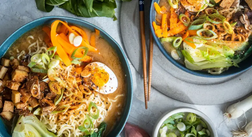 Zwei Schüsseln dampfendes Miso Ramen mit Nudeln, Ei, Karotten, Pak Choi und Frühlingszwiebeln.