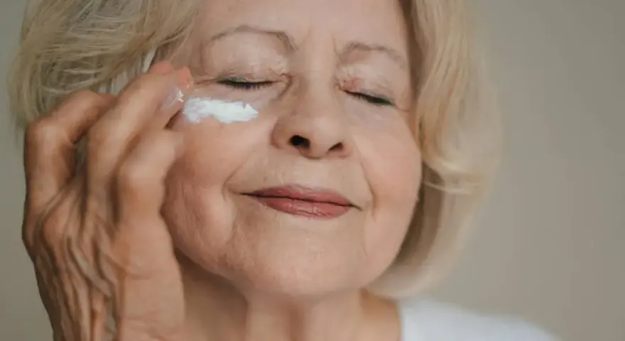 Eine Frau über 70 trägt eine feuchtigkeitsspendende Creme auf. Ihre Augen sind geschlossen, während sie sich um ihre Haut kümmert.