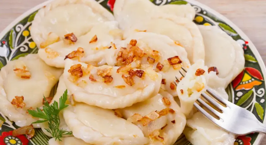 Pyszne pierogi ruskie z farszem Magdy Gessler, posypane skwarkami. Na talerzu z tradycyjnym wzorem.