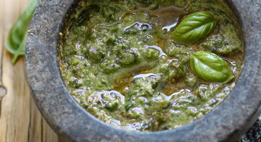 Pesto genovese originale appena preparato nel mortaio, con basilico fresco e olio d'oliva.