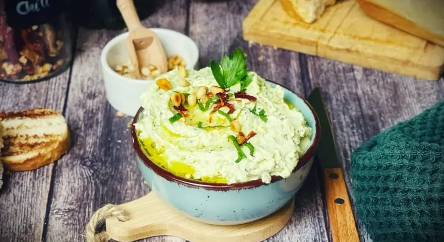 Cremiger Zucchini-Dip mit Pinienkernen und Kräutern, serviert mit geröstetem Brot.