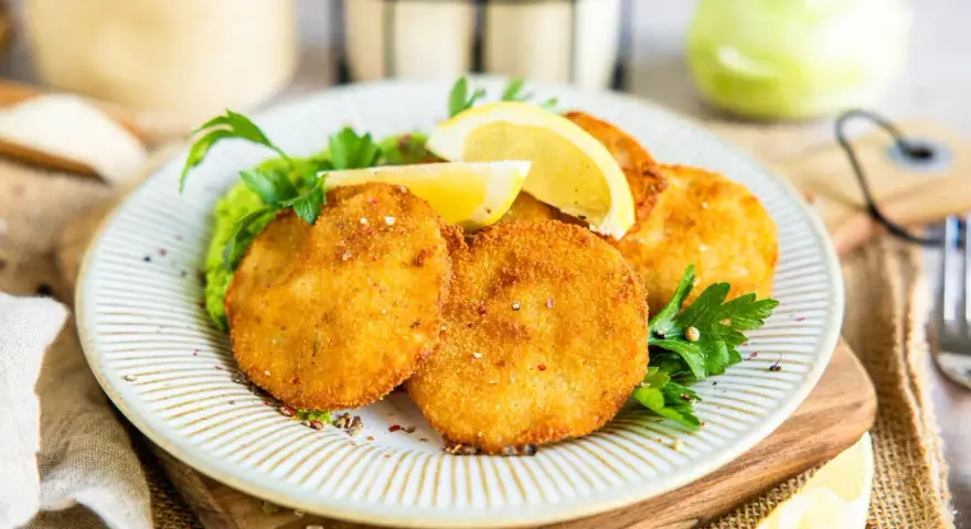 Knusprige Kohlrabi-Schnitzel auf einem Teller mit Erbsenpüree, Zitrone und Petersilie. Ein köstliches vegetarisches Gericht.