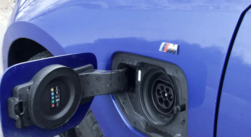Niebieskie BMW 330e z otwartą klapką gniazda ładowania.