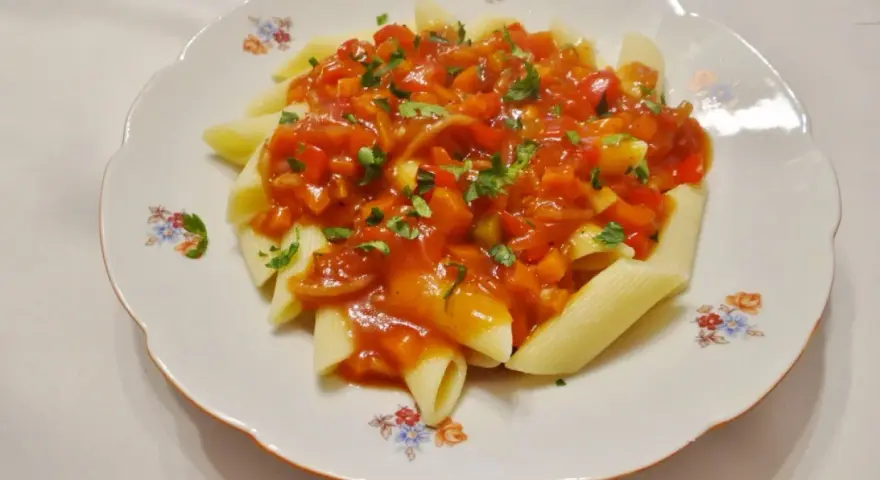 Penne z aromatycznym, słodko-kwaśnym sosem warzywnym, posypane świeżą natką pietruszki.